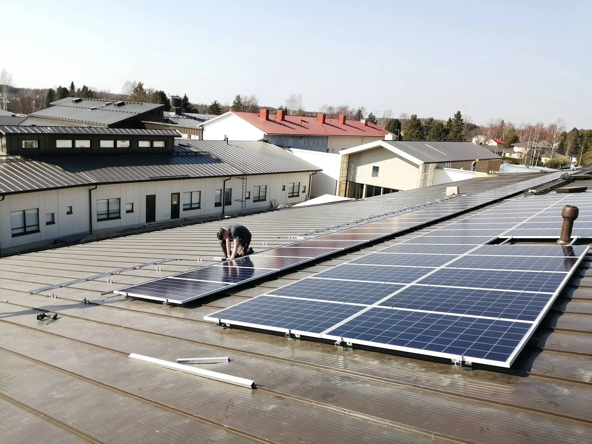 Työntekijä asentaa aurinkopaneeleita suuren rakennuksen metallikatolle osana aurinkovoimalan rakentamista.